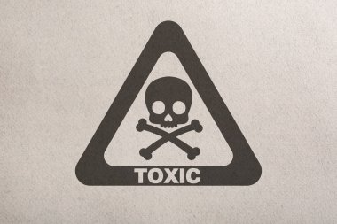 Hazard warning sign (skull-and-crossbones symbol and word TOXIC) on paper, top view