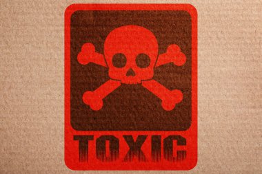 Hazard warning sign (skull-and-crossbones symbol and word TOXIC) on cardboard, top view