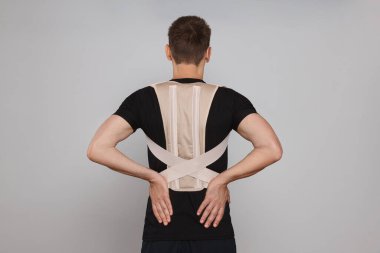 Man with orthopedic corset on grey background, back view