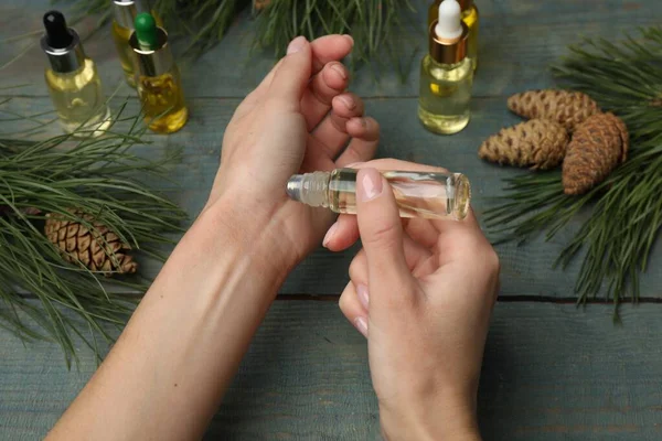 Woman applying pine essential oil on wrist at light blue wooden table, closeup