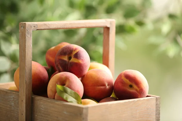 Fresh sweet peaches in wooden crate outdoors, closeup