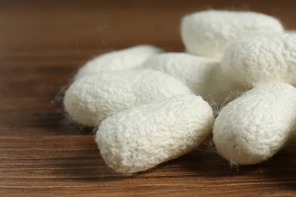 Heap of white silk cocoons on wooden table, closeup
