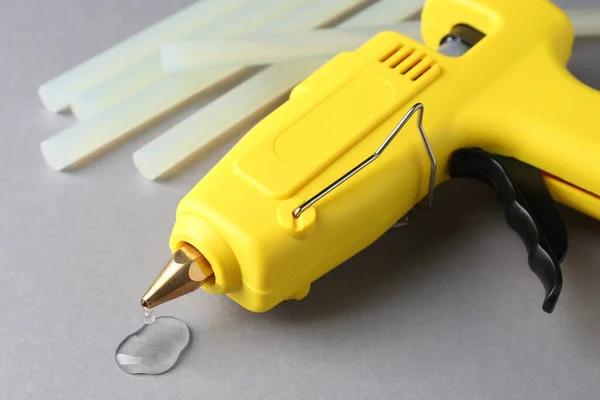 Melted glue dripping out of hot gun nozzle near sticks on grey background, closeup