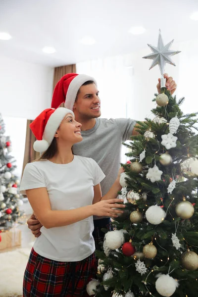 室内に星のトッパーとクリスマスツリーを飾るカップル — ストック写真