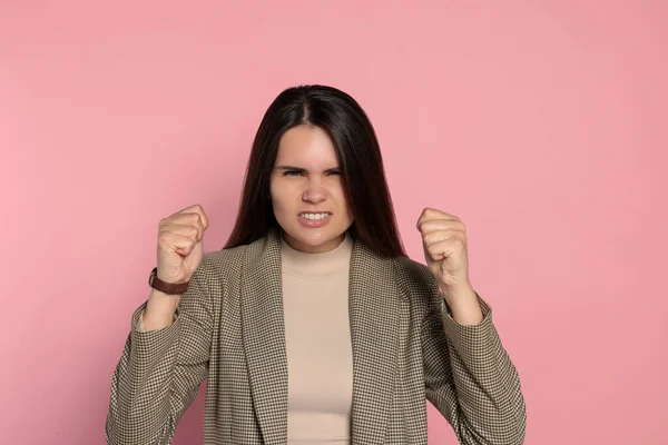 Aggressive young woman showing fists on pink background