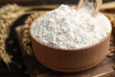 Wheat flour in bowl, spikes and grains on wooden board, closeup