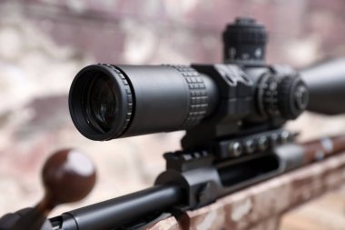 Closeup view of modern powerful sniper rifle with telescopic sight on blurred background