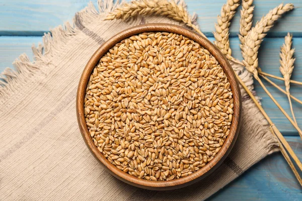 Wheat grains with spikelets on light blue wooden table, flat lay