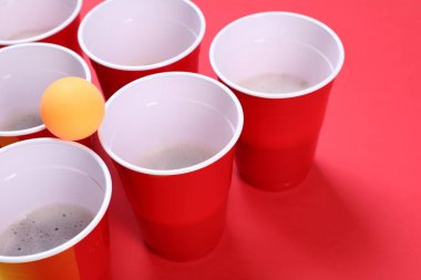 Kırmızı zemin üzerinde bira pongu için plastik bardaklar ve top