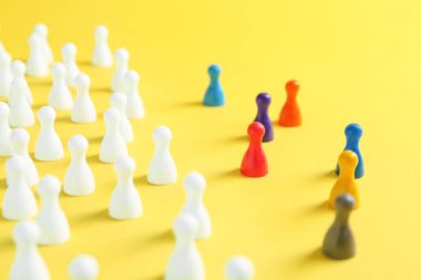 Colorful pawns on yellow background, closeup. Social inclusion concept