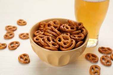 Delicious pretzel crackers and glass of beer on white wooden table, closeup