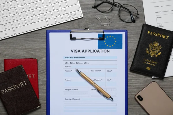 Visa application form for immigration to European Union, passports and stationery on wooden table, flat lay