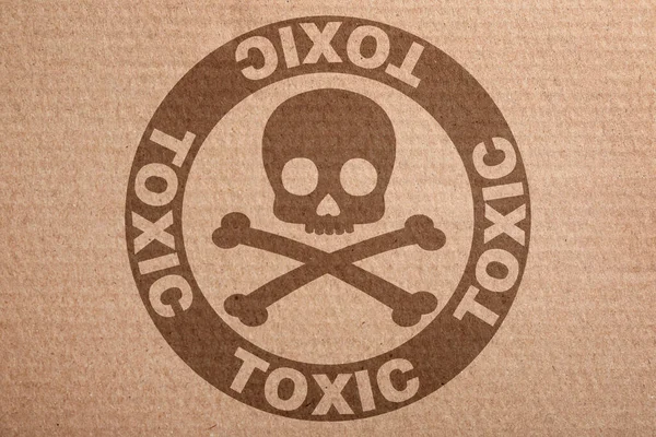 Hazard warning sign (skull-and-crossbones symbol and word TOXIC) on cardboard, top view