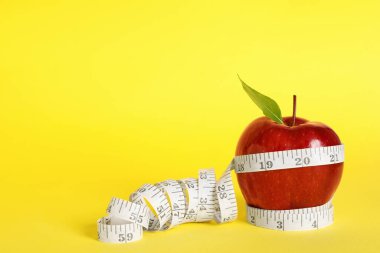 Fresh red apple with measuring tape on yellow background. Space for text
