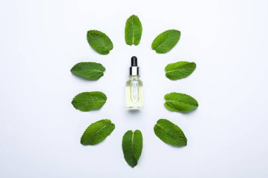 Bottle of essential oil and mint on white background, flat lay
