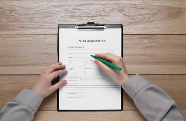 Woman filling visa application form at wooden table, top view