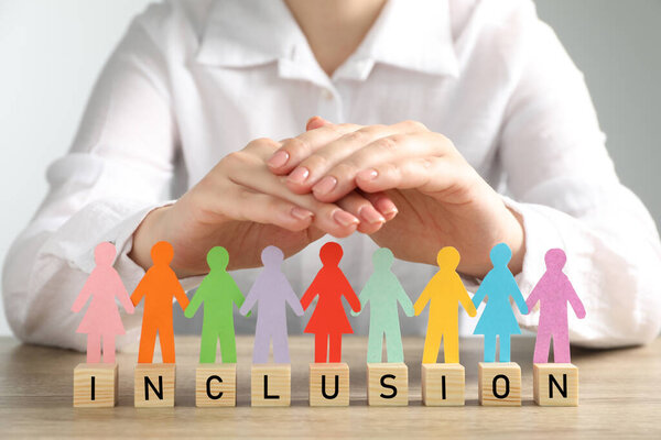 Женщина защищает бумагу человеческие фигуры и деревянные кубики со словом Включение за столом, крупным планом