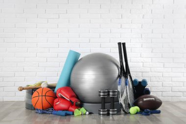 Set of different sports equipment on floor near white brick wall