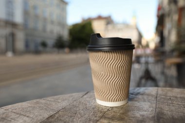 Cardboard takeaway coffee cup with plastic lid on wooden table in city, space for text