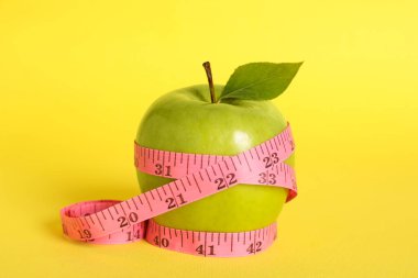 Fresh green apple with measuring tape on yellow background