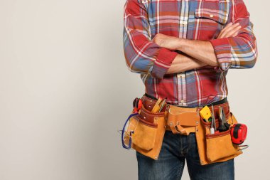 Professional builder with tool belt on light background, closeup. Space for text