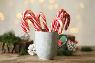 Christmas candy canes in cup on wooden table against blurred lights
