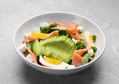 Delicious salad with boiled egg, salmon and avocado on light grey marble table, closeup