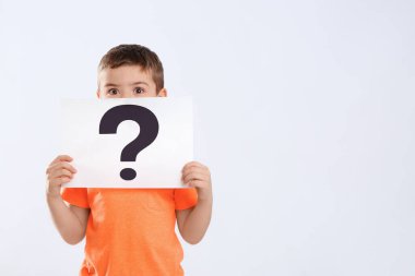 Beyaz arka planda soru işareti olan duygusal küçük çocuk elinde kağıt tutuyor.