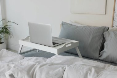 White tray table with laptop on bed indoors