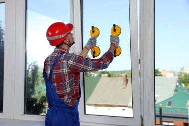 Worker using suction lifters during plastic window installation indoors