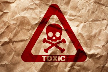 Hazard warning sign (skull-and-crossbones symbol and word TOXIC) on crumpled kraft paper, top view