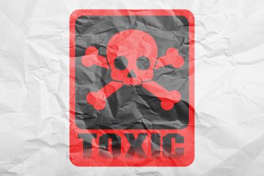 Hazard warning sign (skull-and-crossbones symbol and word TOXIC) on crumpled white paper, top view