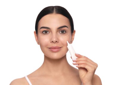 Beautiful young woman applying gel on skin under eye against white background