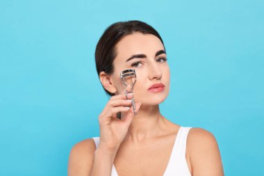 Woman using eyelash curler on turquoise background