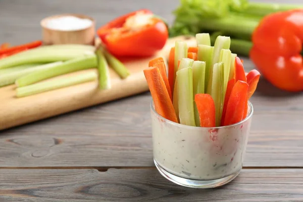 Celery and other vegetable sticks with dip sauce in glass bowl on wooden table. Space for text