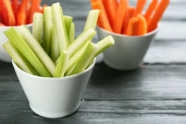 Celery and other vegetable sticks in bowls on grey wooden table, closeup