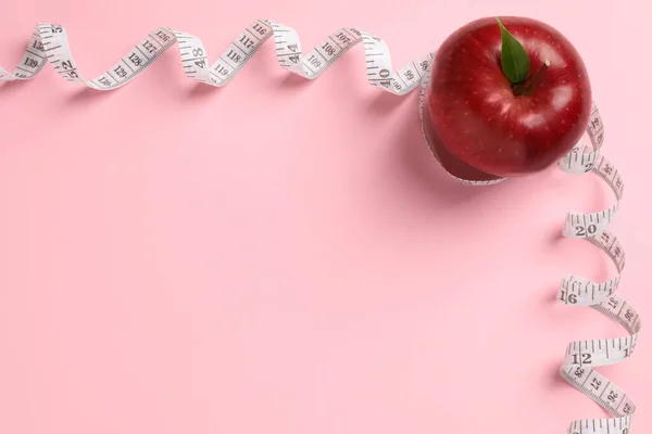 Fresh red apple with measuring tape on pink background, flat lay. Space for text