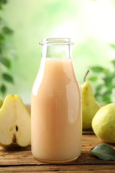Fresh pear juice in glass bottle and fruits on wooden table, closeup