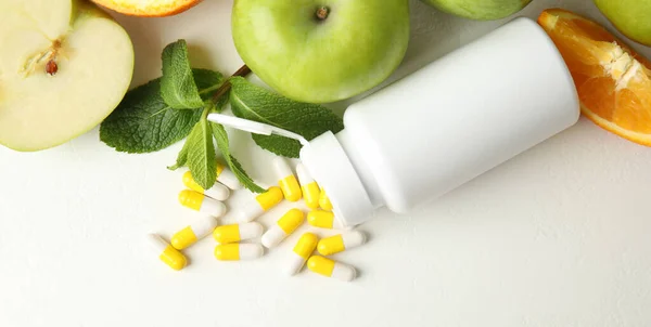 Bottle with vitamin pills and fruits on white table, flat lay. Space for text