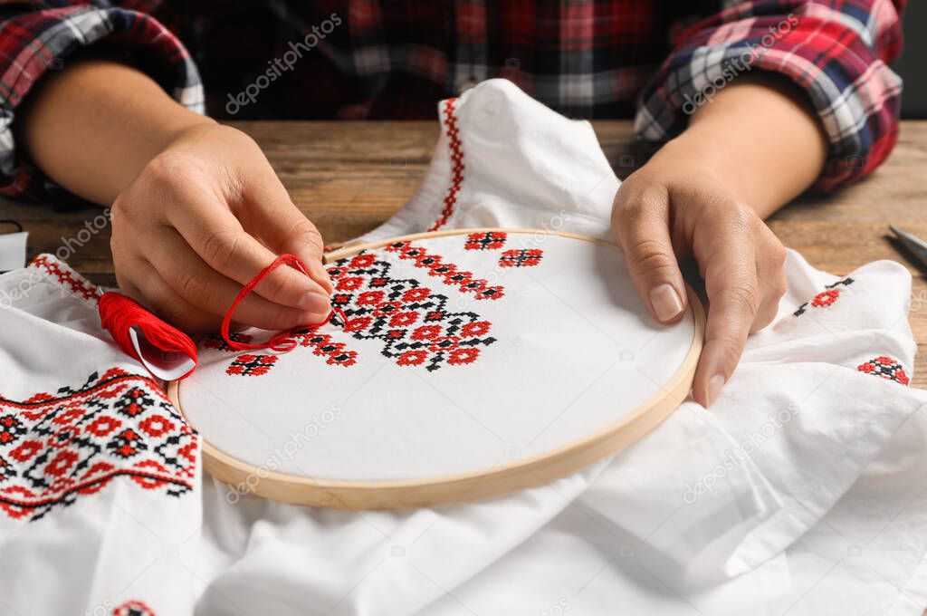 Woman embroidering white shirt with colorful threads at wooden table, closeup. Ukrainian national clothes