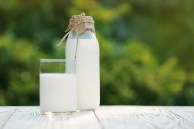 Bottle and glass of tasty fresh milk on white wooden table against blurred background, space for text