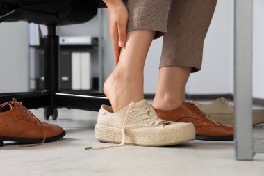 Rahatsız ayakkabılarını çıkaran ve ofiste spor ayakkabılarını giyen bir kadın.