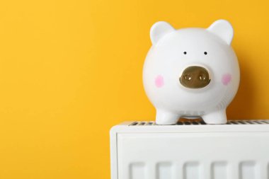 Piggy bank on heating radiator against orange background, space for text
