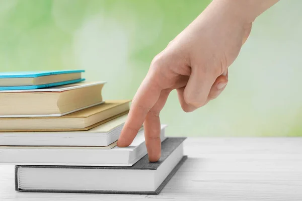 Man climbing up stairs of books with fingers on white wooden table against blurred background, closeup