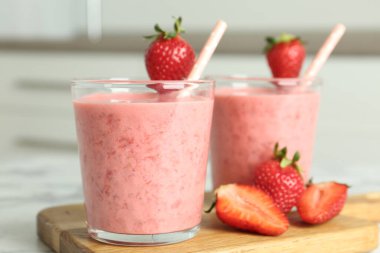 Tasty strawberry smoothies in glasses on wooden board, closeup