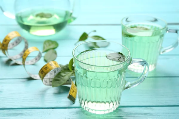 Herbal diet tea and measuring tape on light blue wooden table