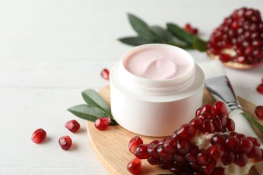Jar with natural facial mask, pomegranate seeds and green leaves on white table, closeup