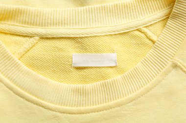 Blank clothing label on yellow sweater, top view