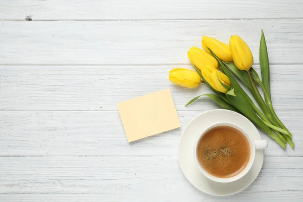 Yellow tulips, coffee and blank card on white wooden table, flat lay with space for text. Good morning