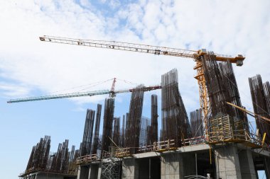 Tower cranes near building under construction against cloudy sky